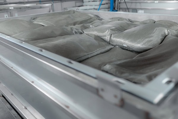 Graue, industrielle Edelstahlwanne voller ungeöffneter Säcke mit grauem Pulver, detailreich.